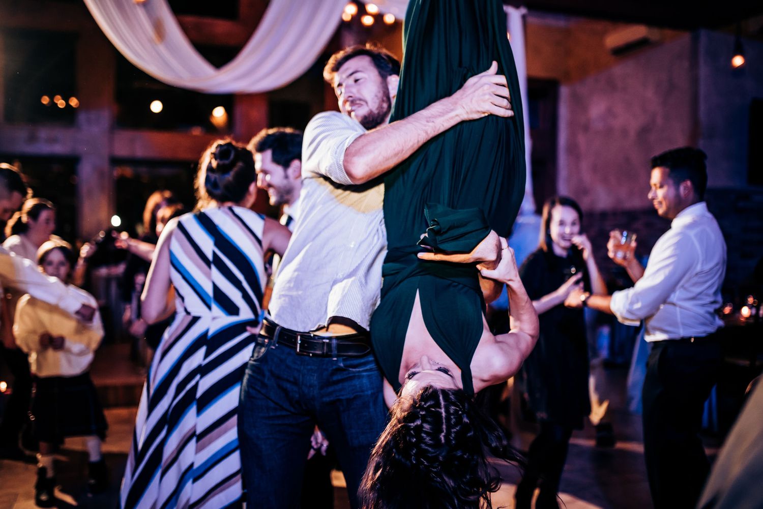 Energetic dancers perform swing moves on a dimly lit dance floor with string lights and fabric decor.