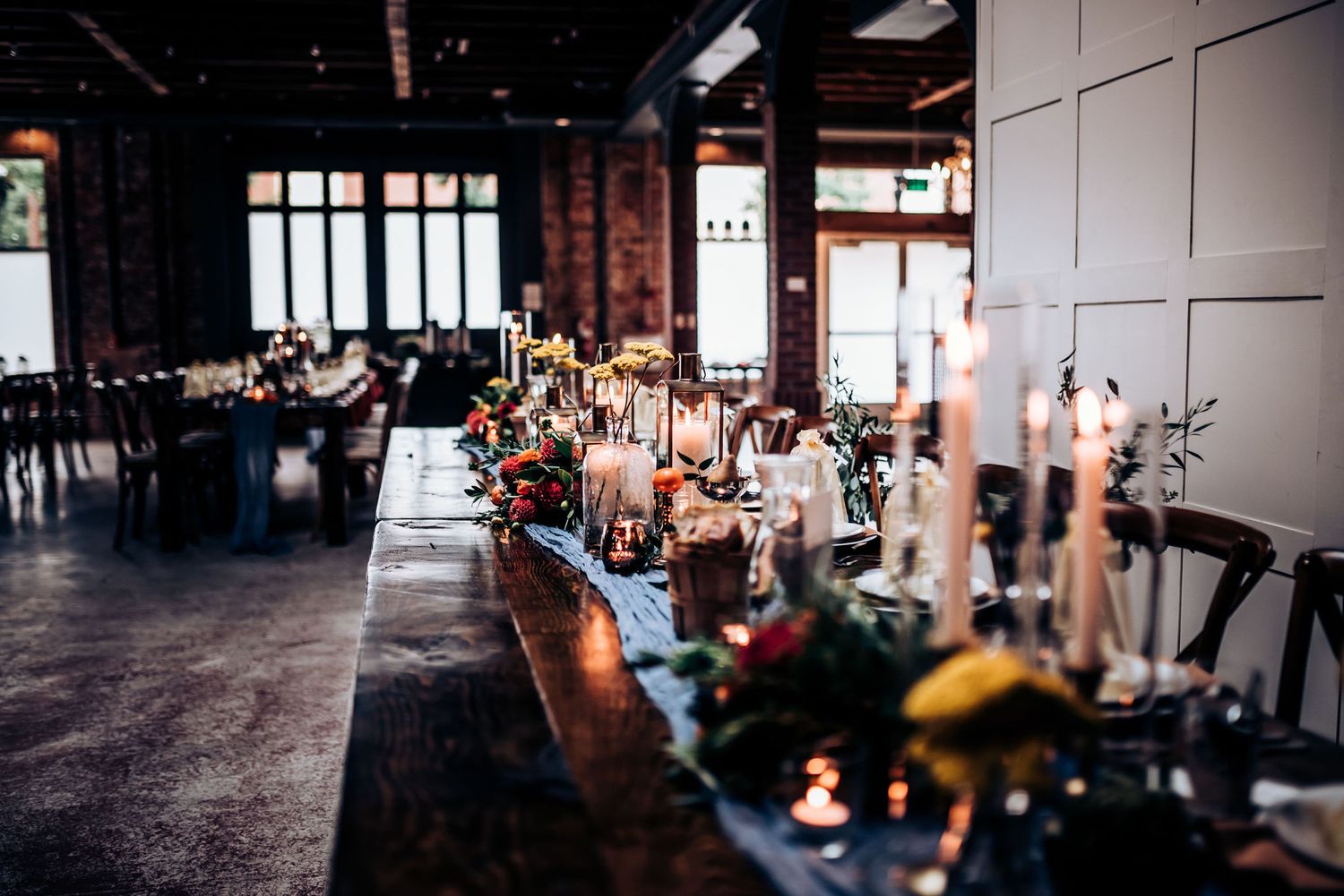 Wedding reception table with vintage-inspired decor, candles and floral arrangements in dark venue.