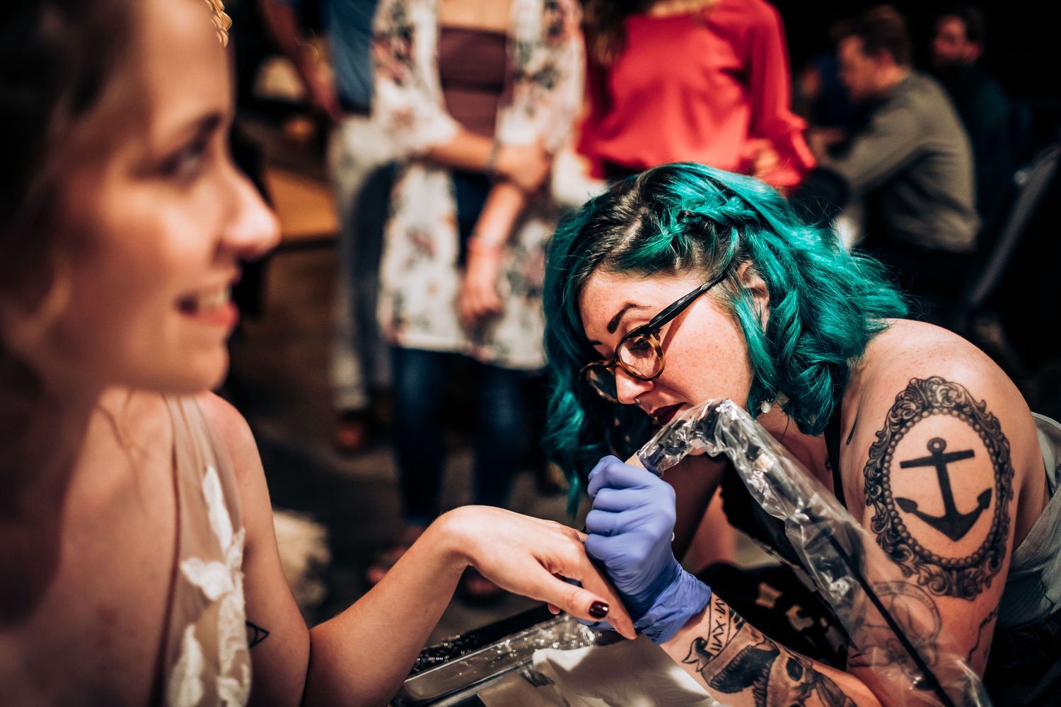 Artist with vibrant teal hair creates custom designs for wedding guests.