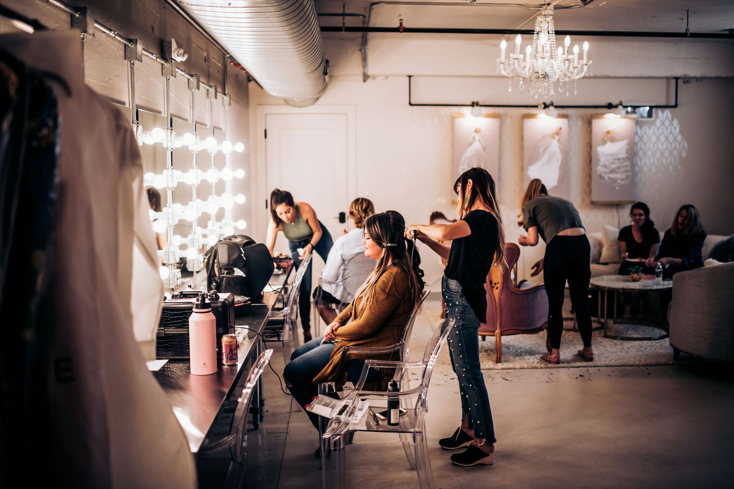 Professional makeup artists working in a stylish salon with vanity lights and chandeliers.