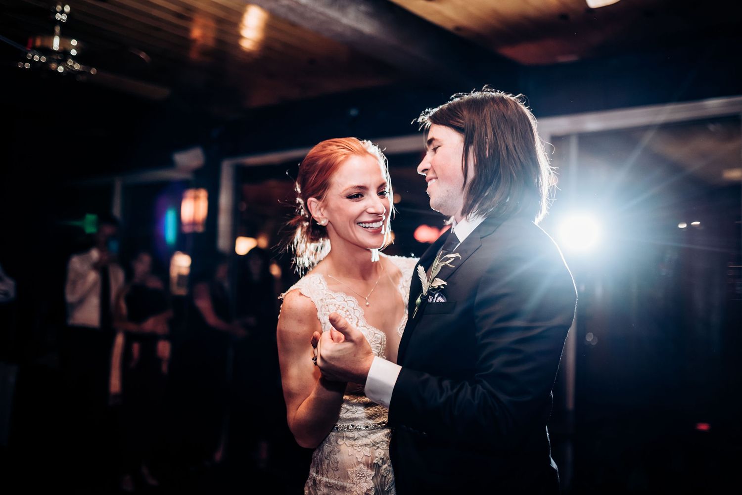 A couple shares a joyful moment while dancing in a dimly lit reception venue.