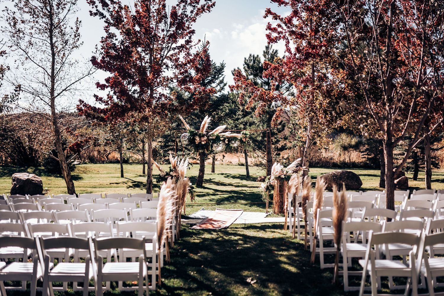 Rows of white chairs set up for an outdoor autumn wedding ceremony with red-leaved trees in the background.