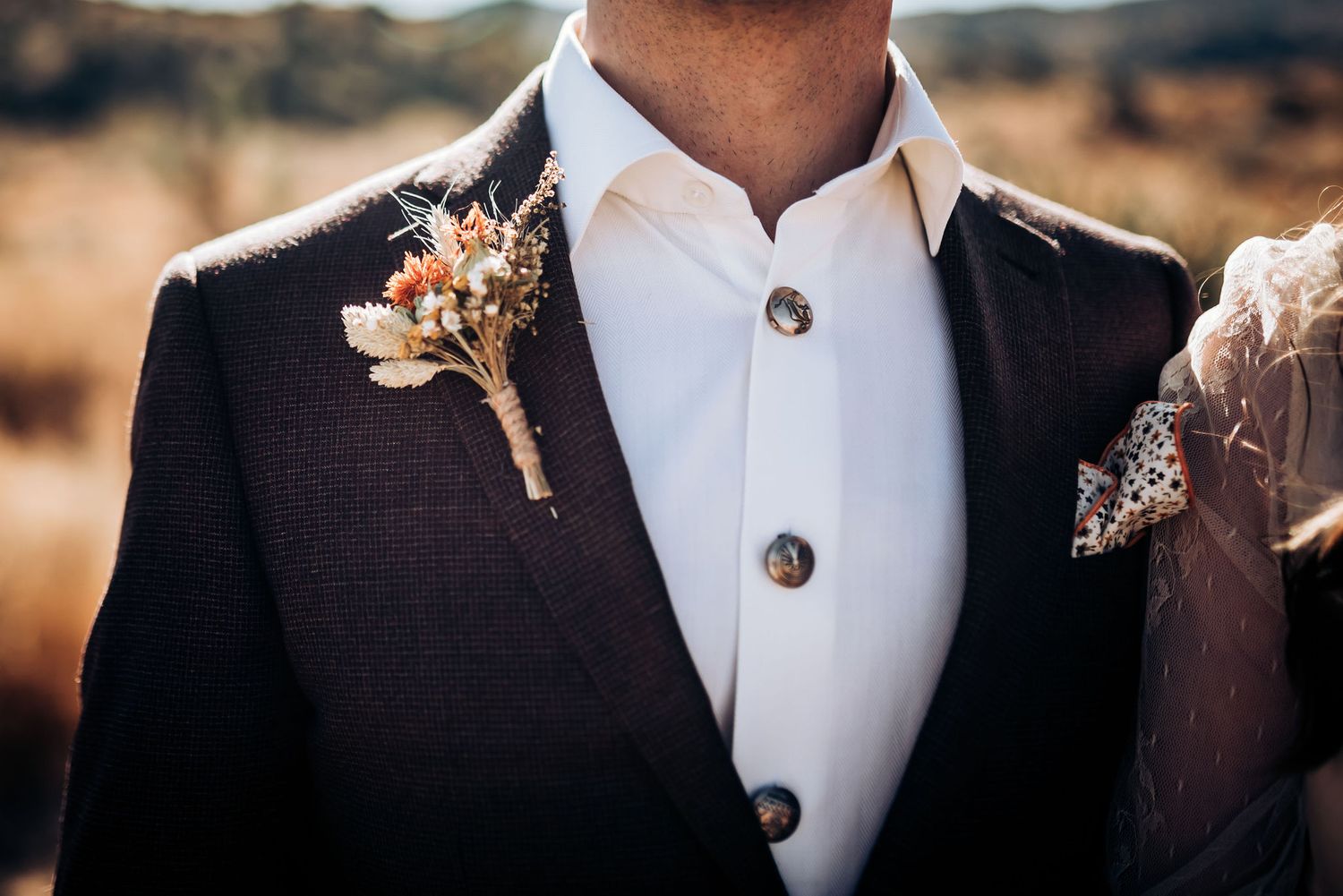 Detail shot of groom's boutonniere and black suit jacket with white dress shirt.