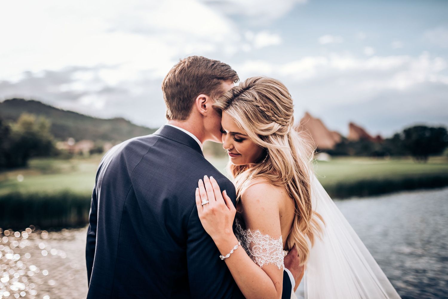 Romantic lakeside wedding moment with flowing veil and mountain backdrop.