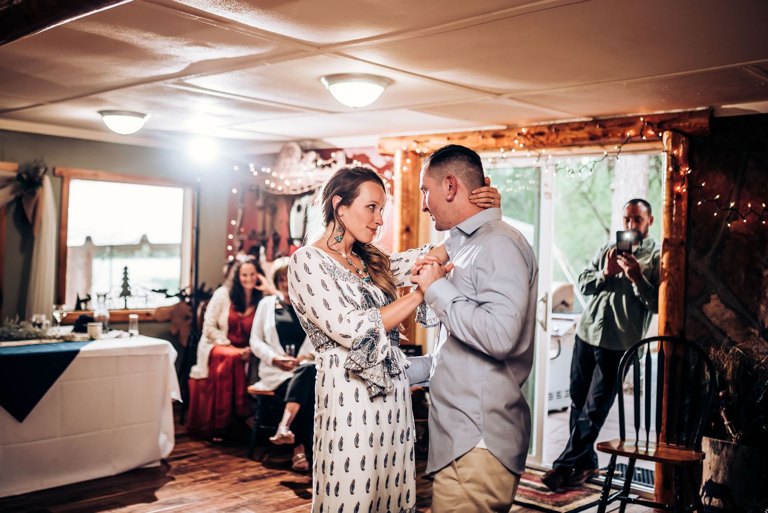 A couple feeding each other cake during their wedding reception while guests look on.