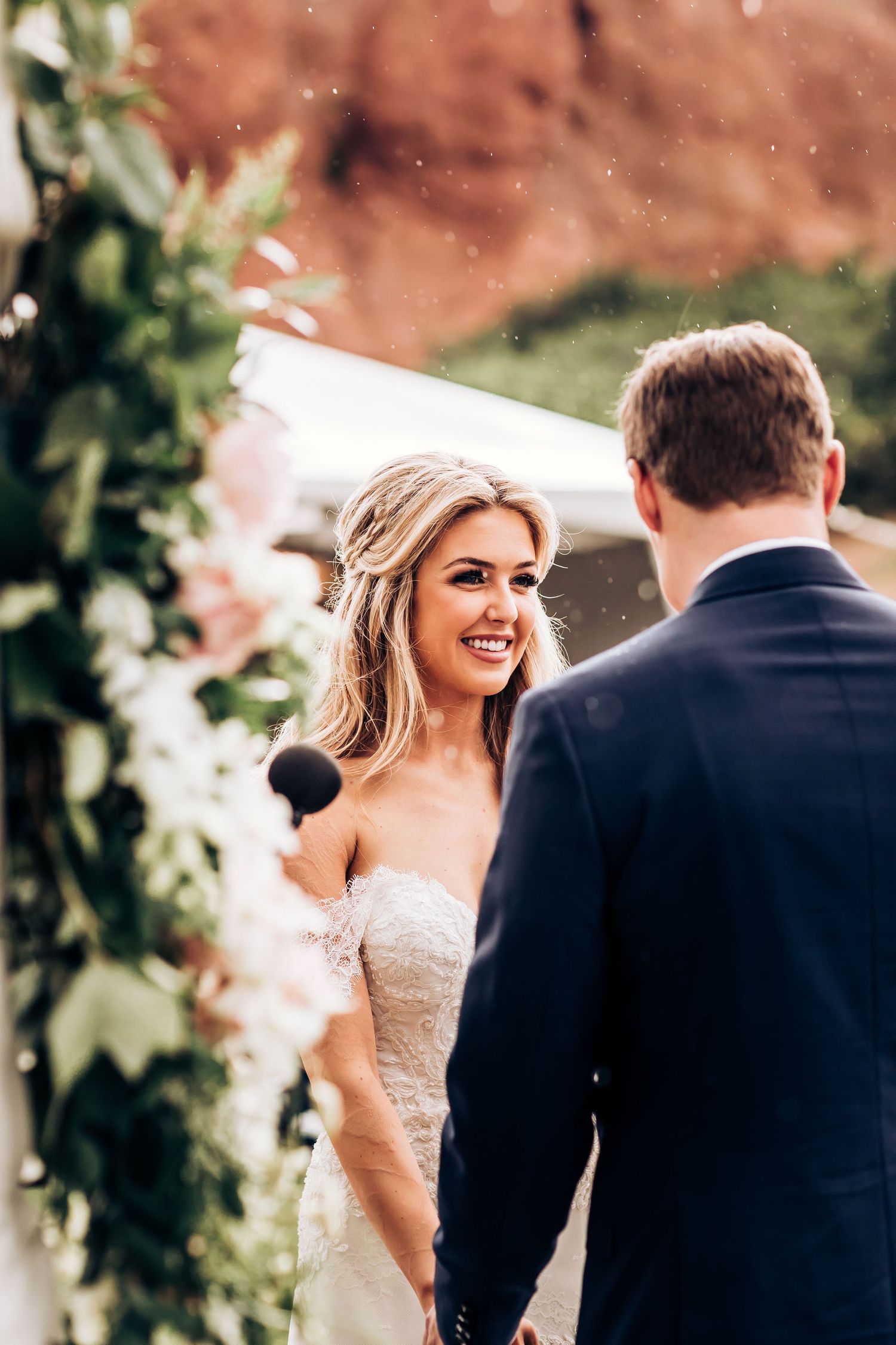 Romantic outdoor wedding ceremony moment between couple under floral arch with red rock formations in background.