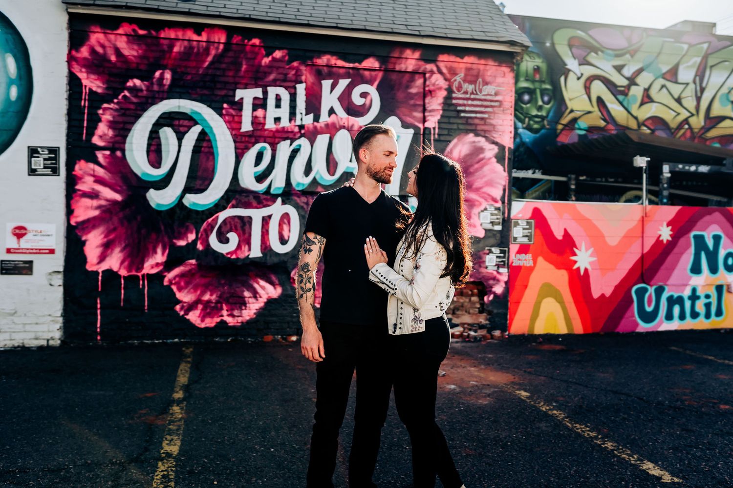 Couple shares intimate moment in front of pink floral graffiti wall.