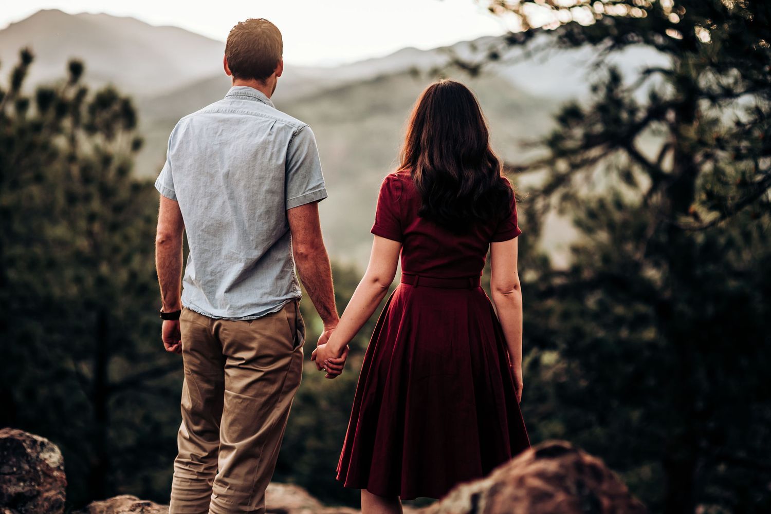 A couple holds hands while overlooking a mountainous landscape at sunset.