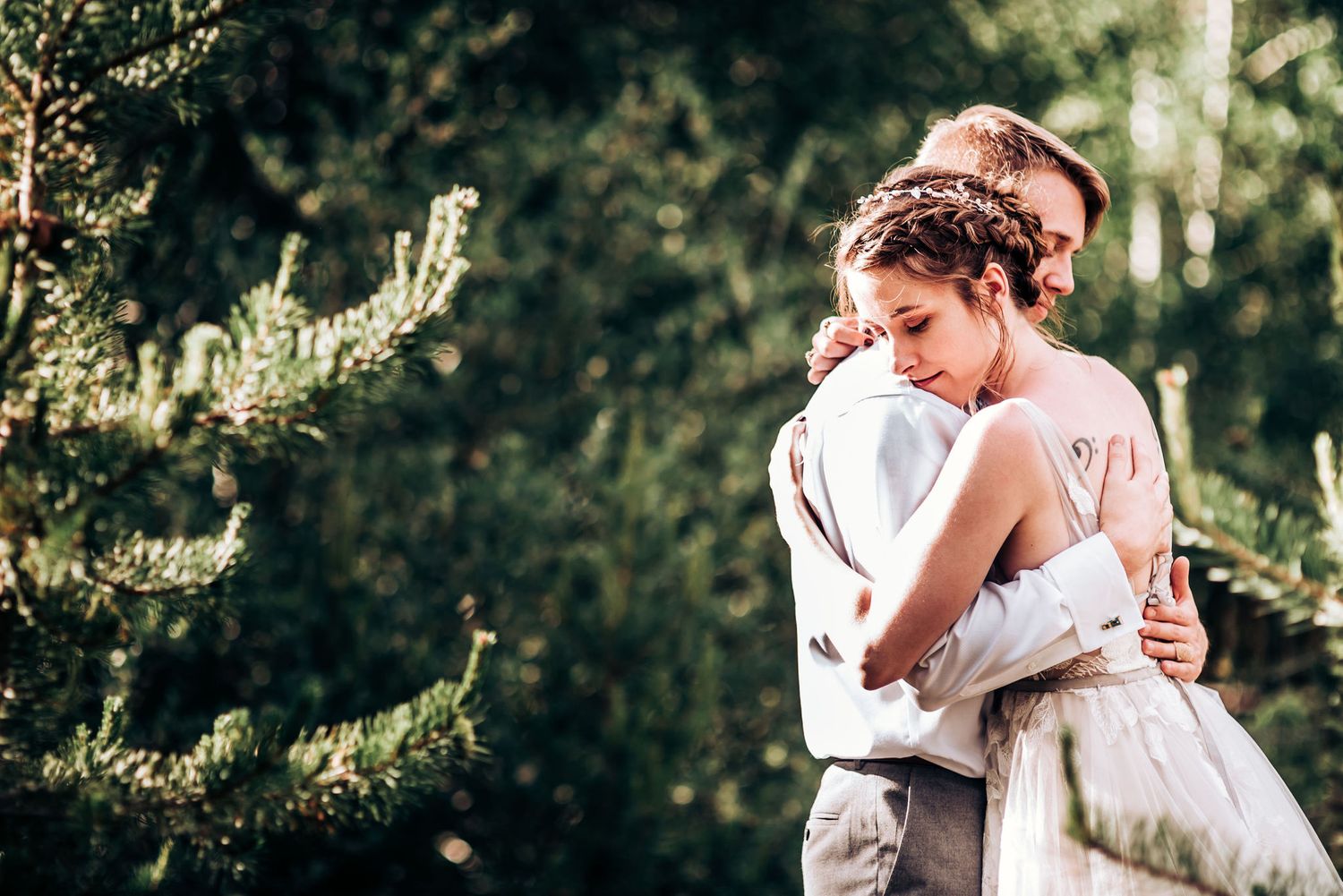 An intimate embrace between newlyweds in a sun-dappled forest setting.