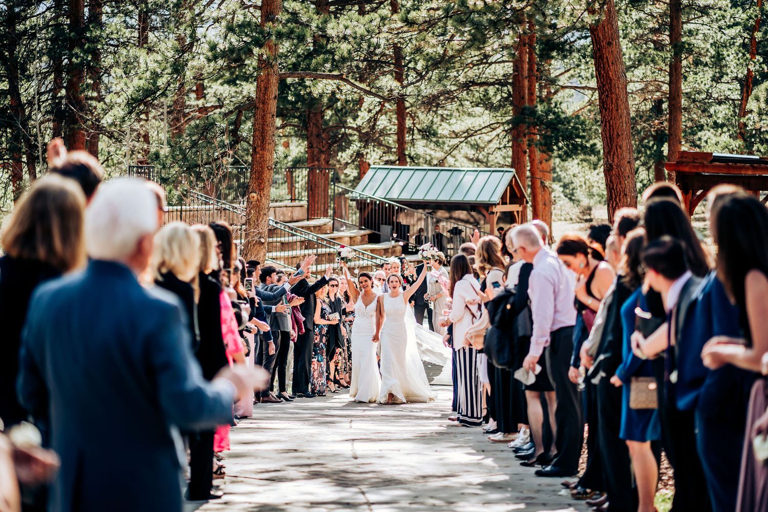 Wedding guests form an aisle in a wooded outdoor setting as they celebrate the newlyweds.