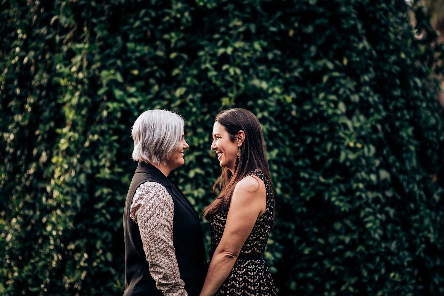Two people share an intimate moment against a wall of green foliage.
