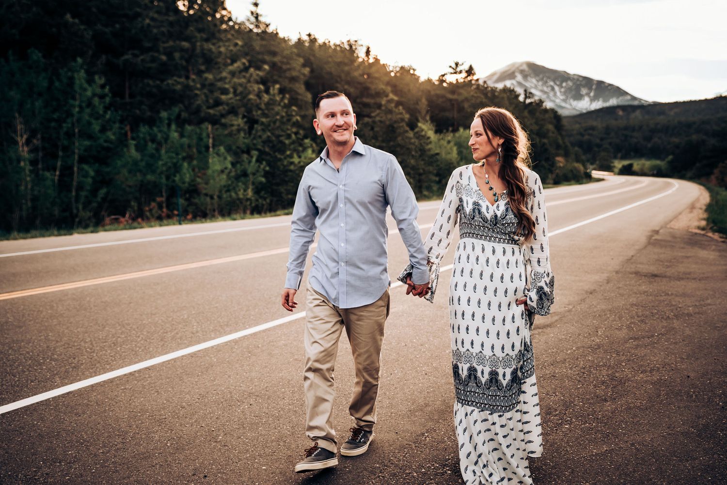 A couple walks hand in hand down a scenic mountain road during golden hour.