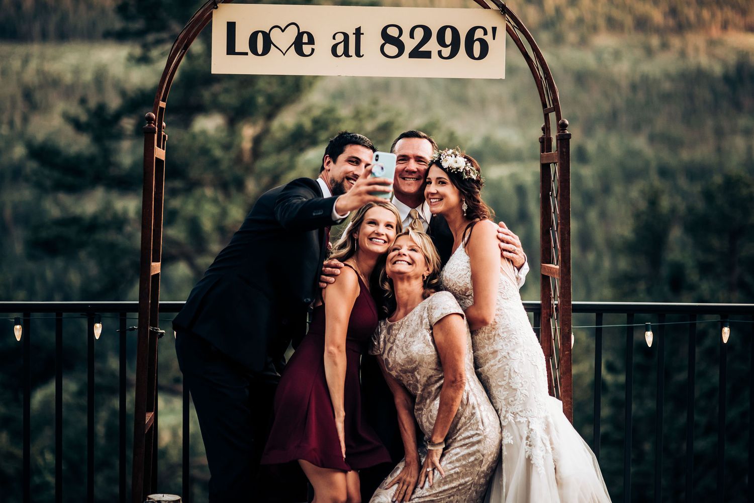 Wedding party poses together under rustic arch with 'Love at 8296' sign.