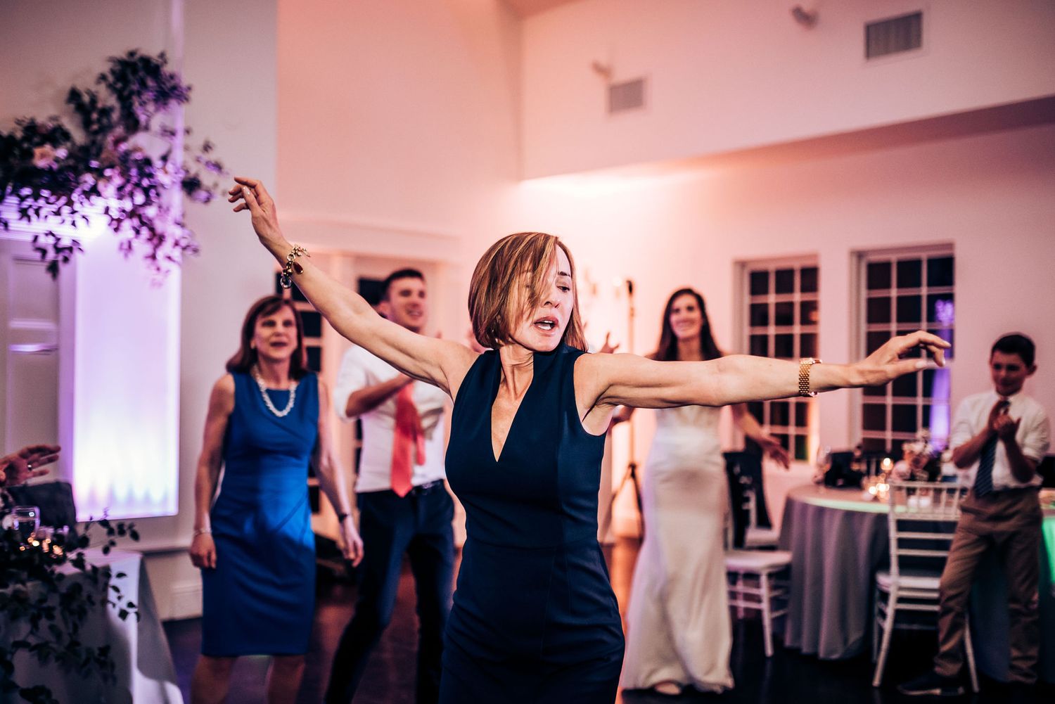 Energetic dancers move to the music at an indoor wedding reception with mood lighting.