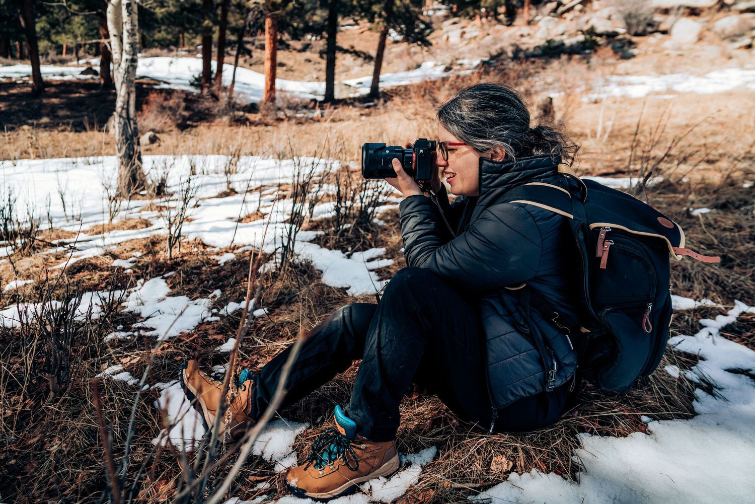 Photographer in snowy terrain capturing nature shots with professional camera equipment in winter landscape.