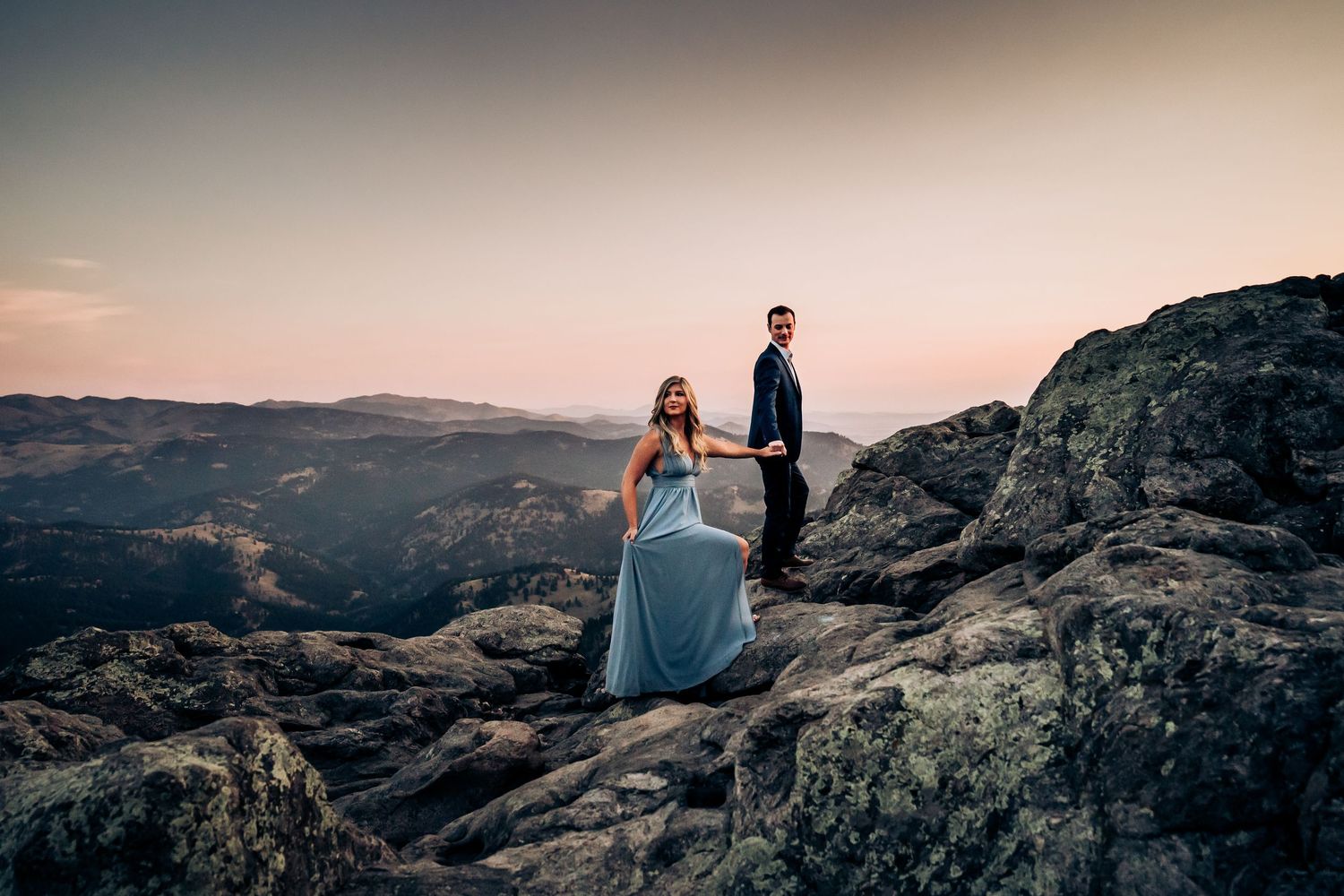Couple standing on rocky mountain overlook during golden hour.