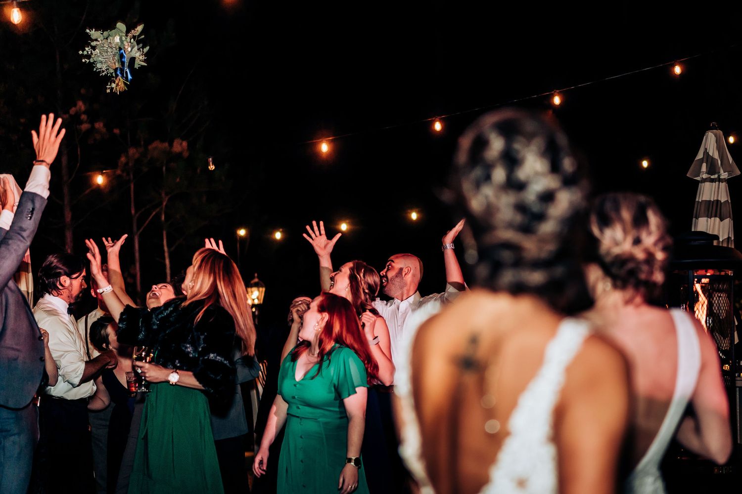 Wedding guests dancing and raising hands during nighttime outdoor celebration.