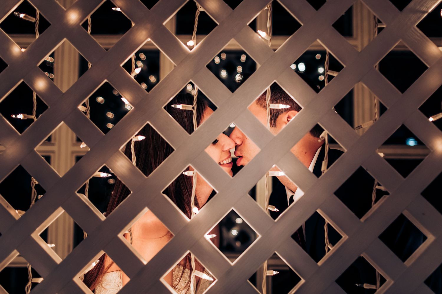 Creative wedding photo through decorative lattice with string lights creating a romantic ambiance.