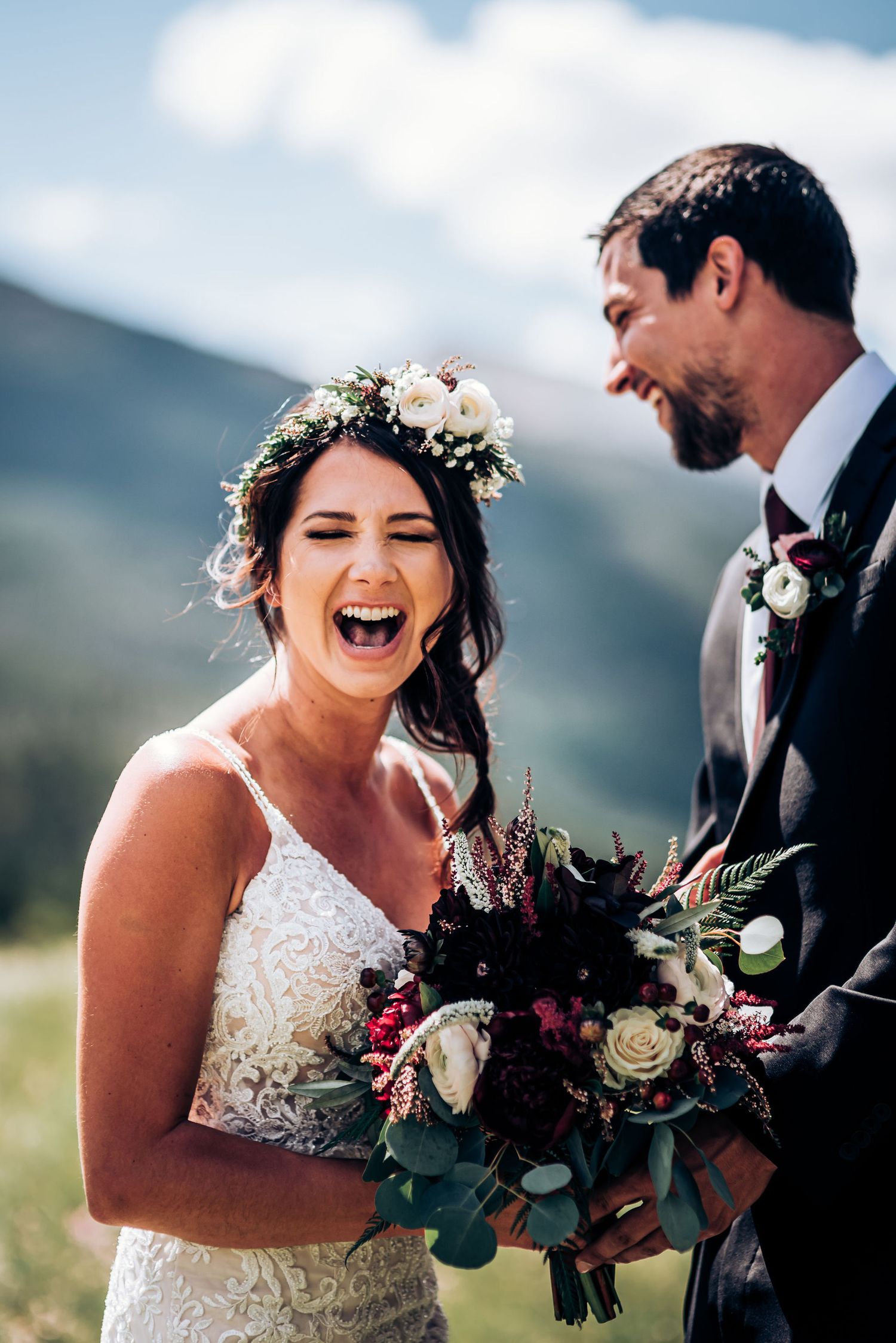 Joyful bride laughs while holding bouquet during outdoor mountain wedding photoshoot.