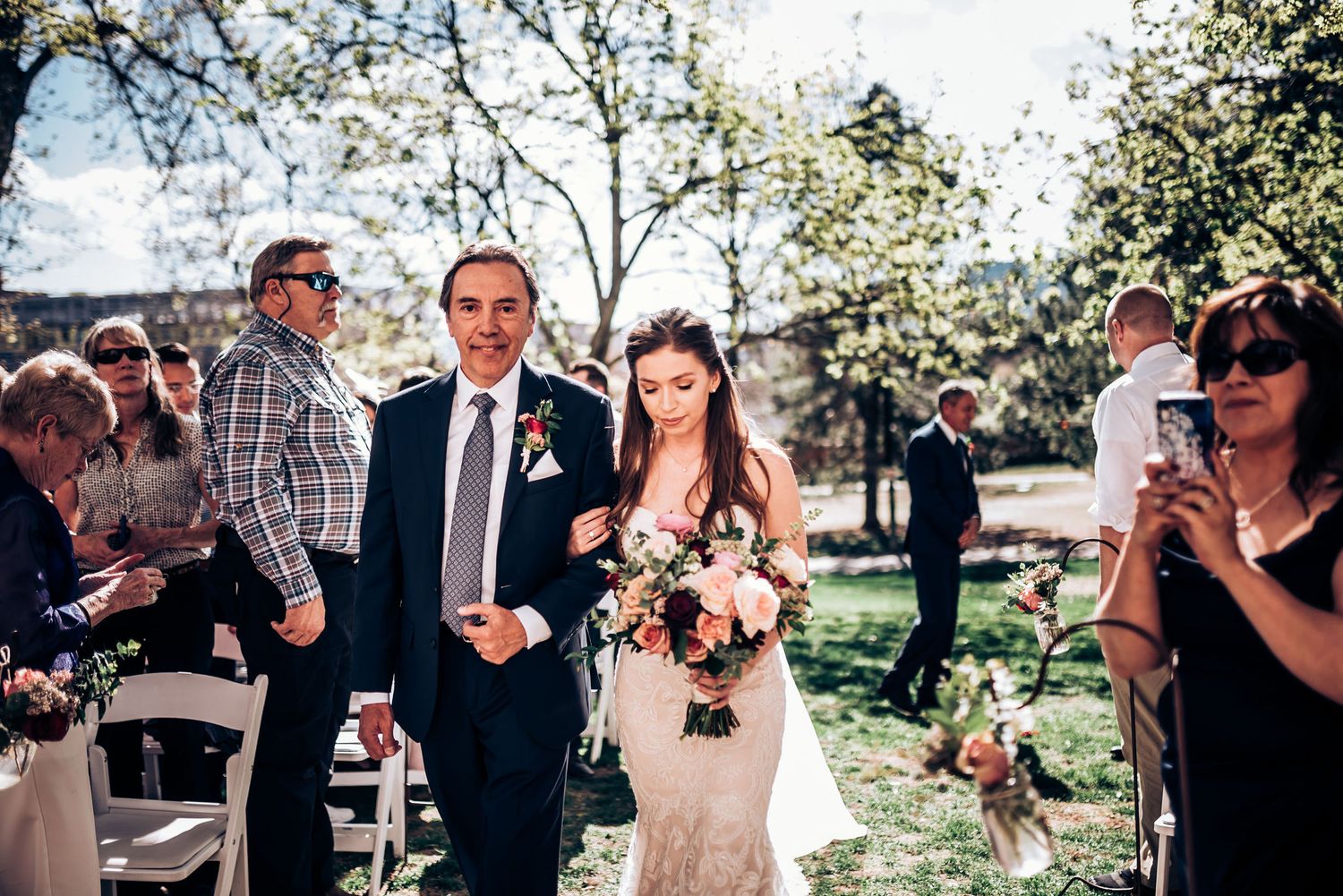 Bride holding a bouquet walks down the outdoor wedding aisle during a spring ceremony.