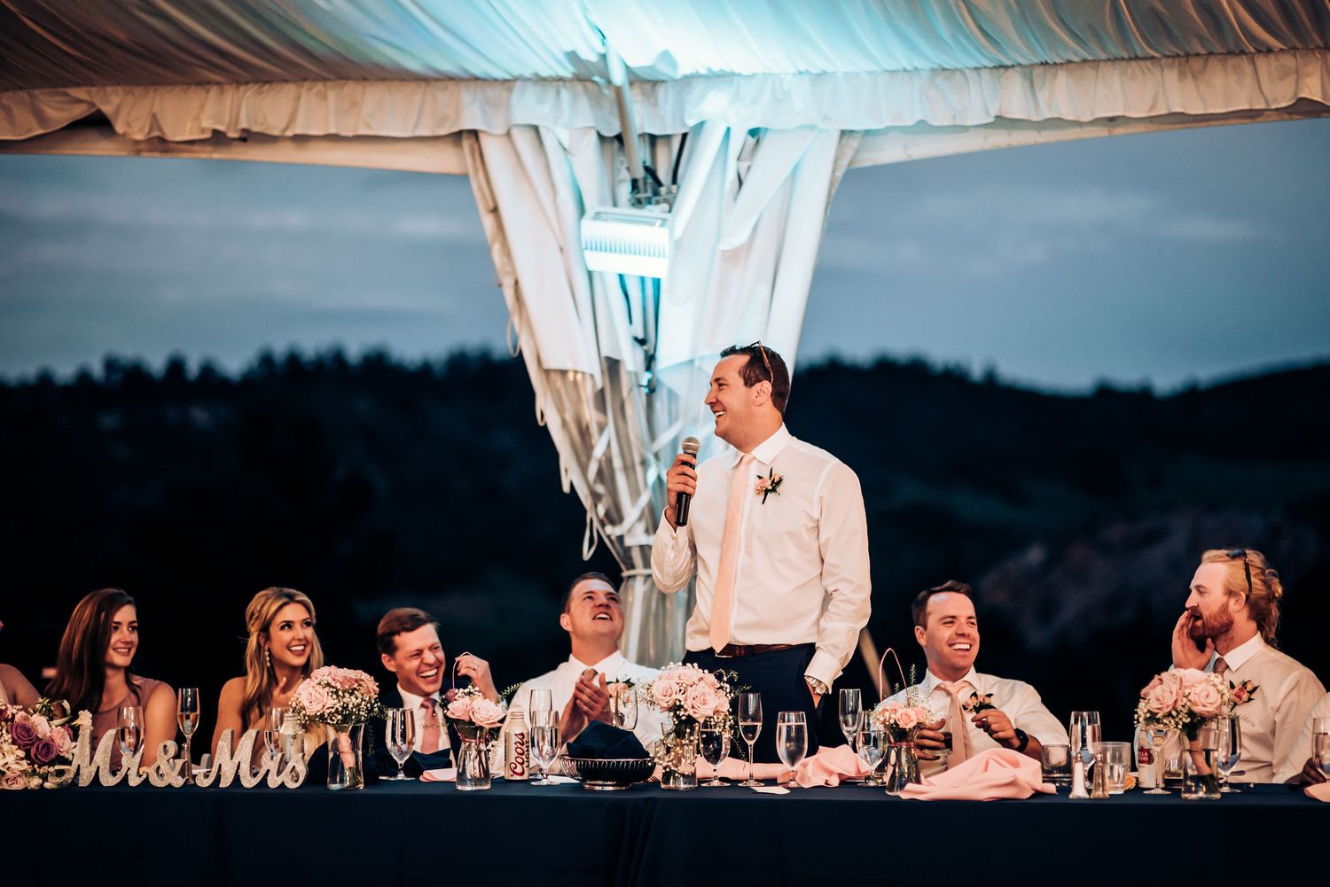 Evening wedding reception with head table under tent lighting.