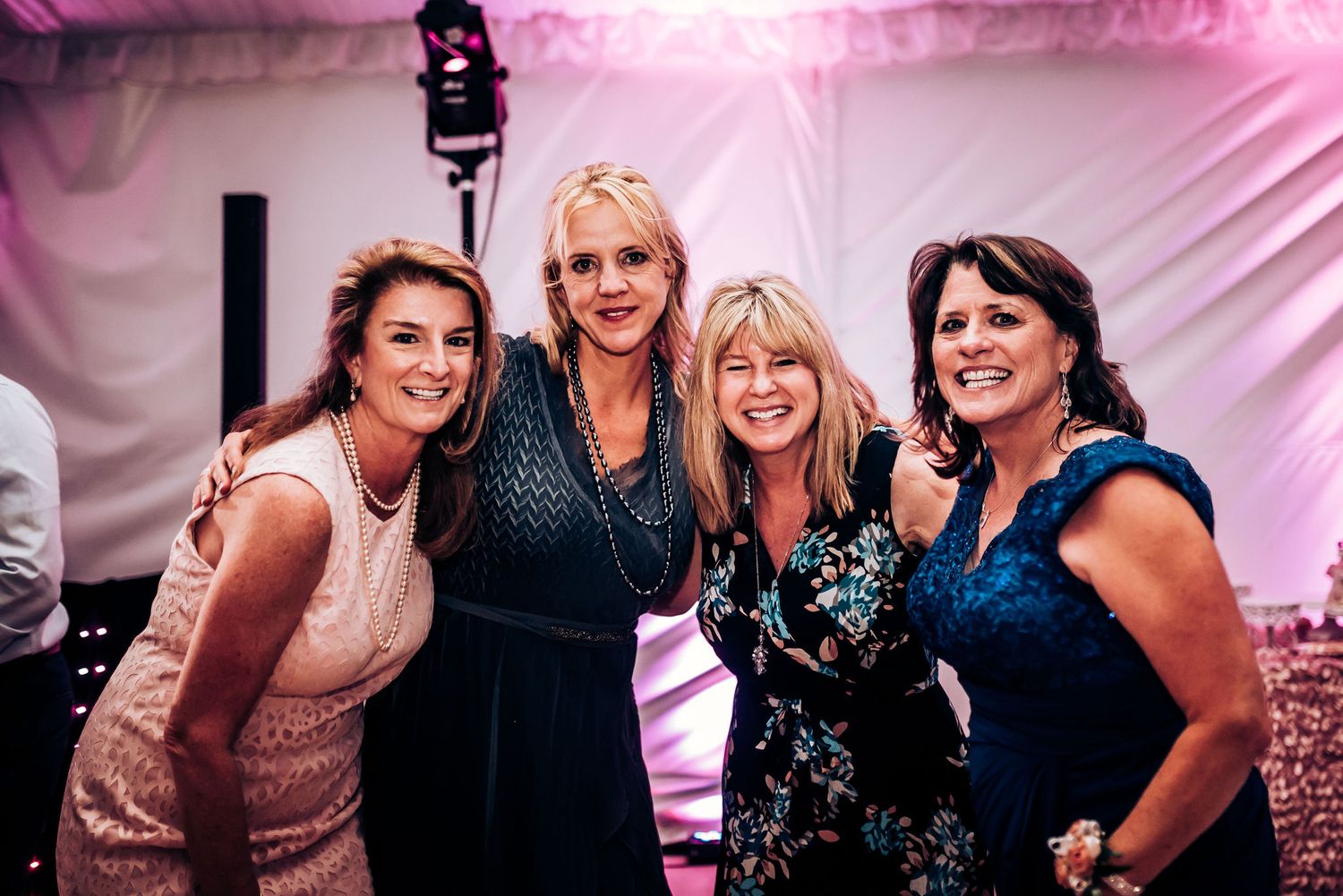 Group of friends pose together at a wedding reception with pink lighting effects.