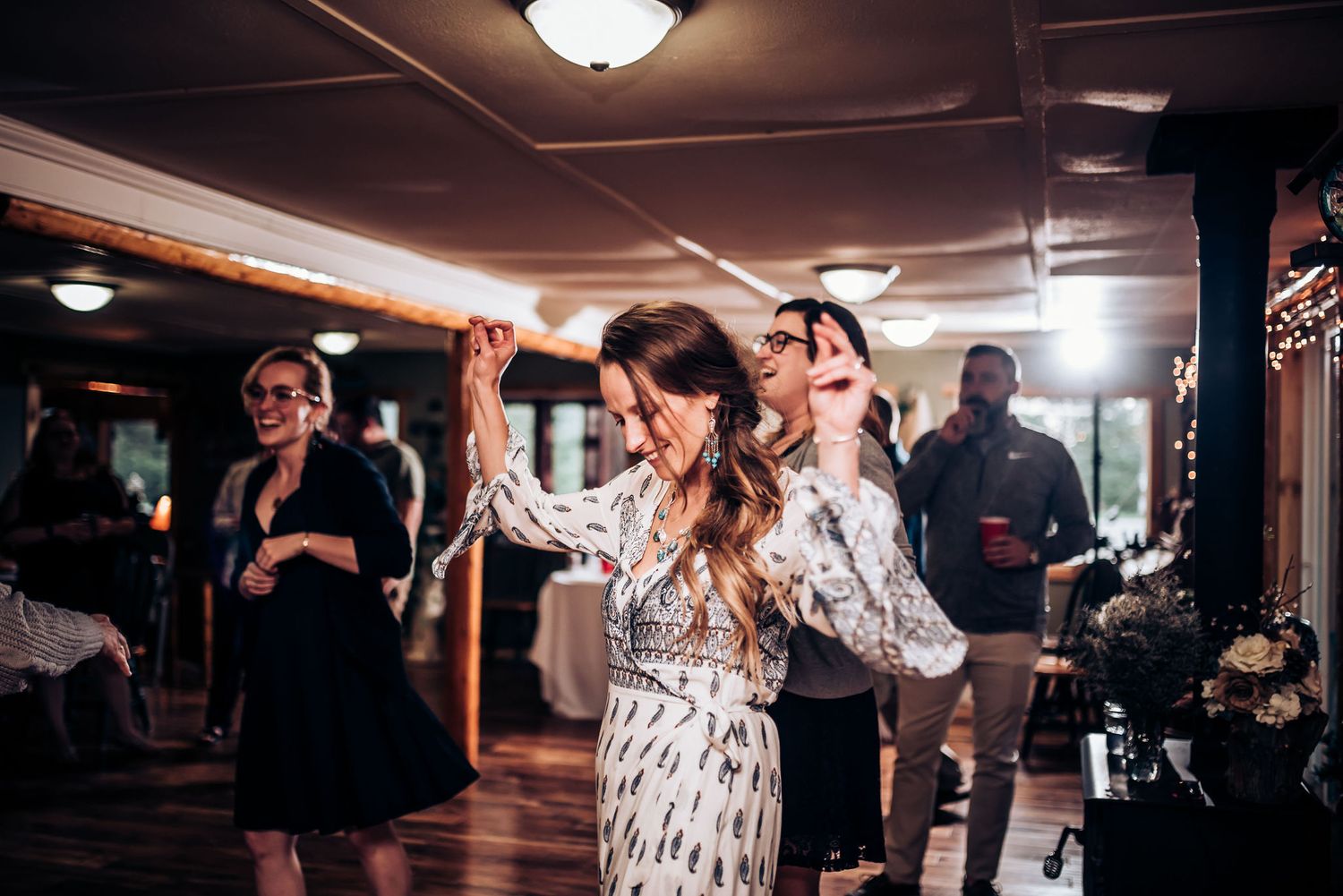 People dance and celebrate at a dimly lit indoor venue with wooden walls and floor.