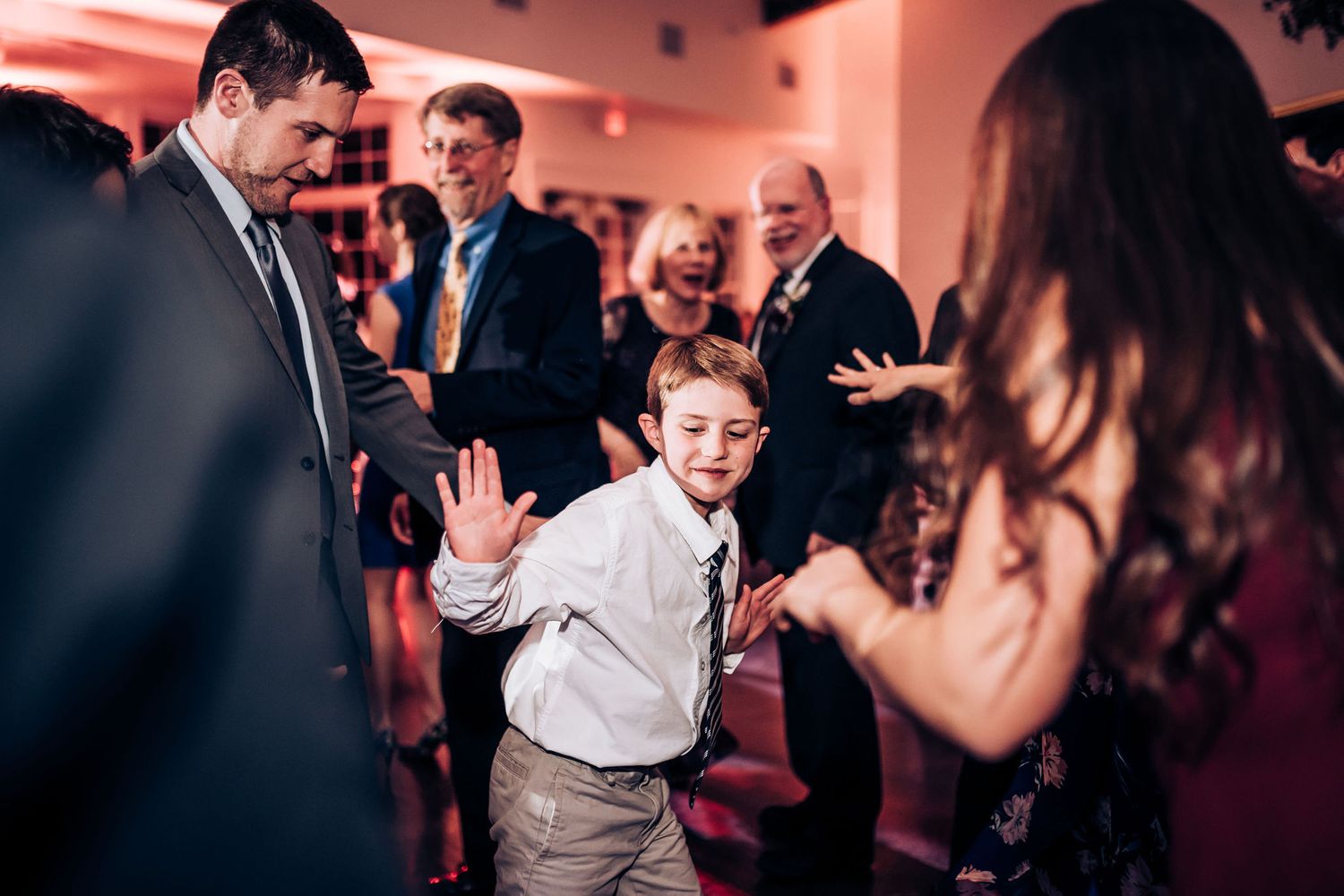 Young attendee shows off dance moves at a wedding reception with pink lighting.