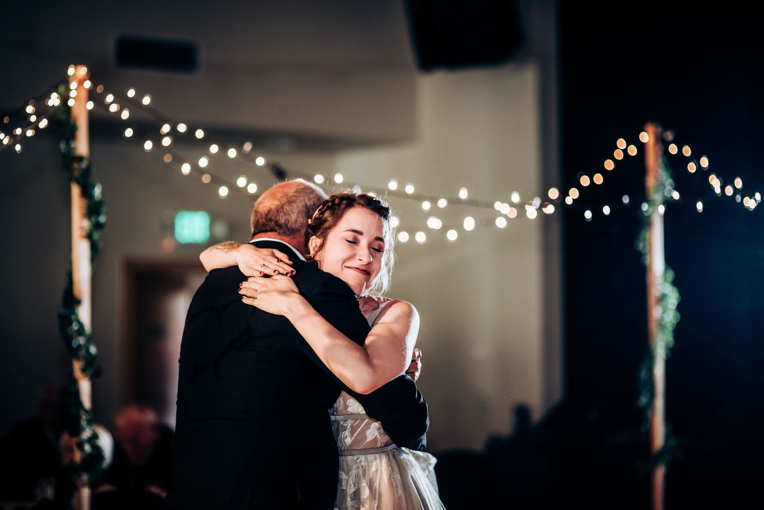 Couple sharing an intimate dance beneath twinkling string lights at an indoor wedding reception.