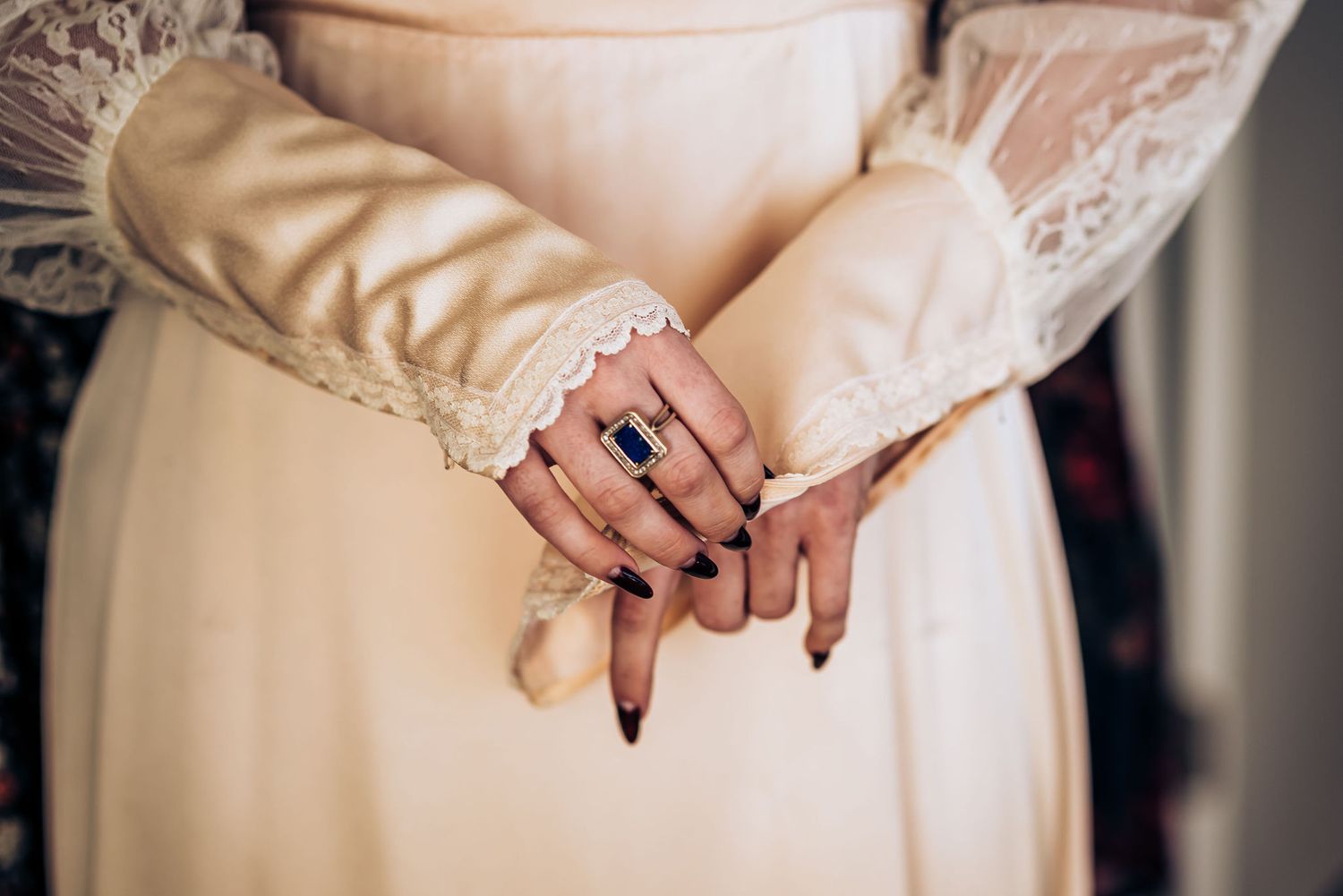 Detail shot of hands wearing a sapphire engagement ring against a vintage-style lace dress.