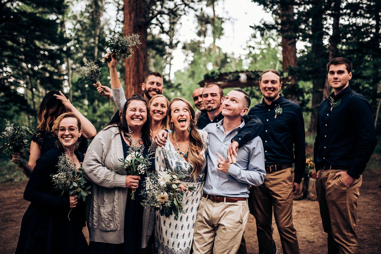 Wedding party celebrates with joyful expressions in a forest setting at sunset.