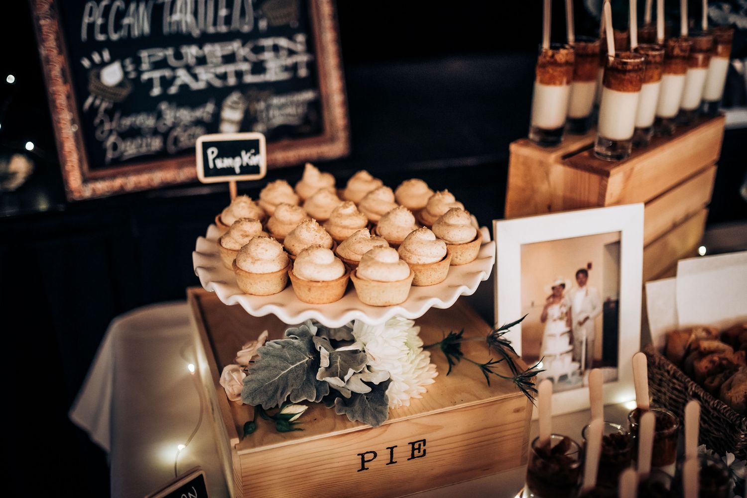 Wooden pie box filled with cupcakes next to chalkboard menu and dessert display.