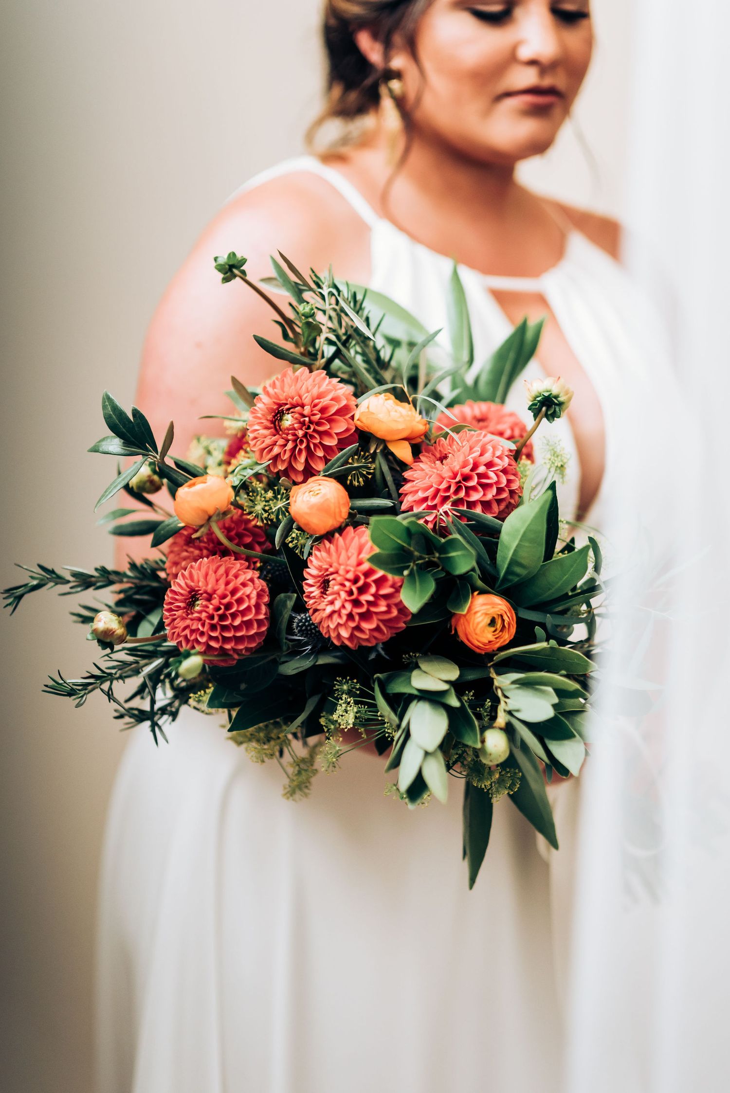 Close-up of coral and orange wedding bouquet with dahlias and greenery.