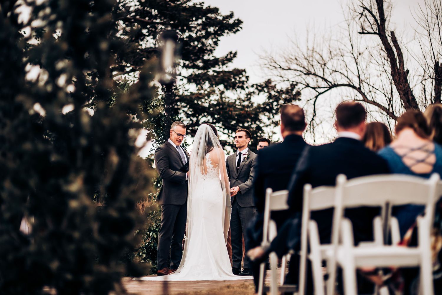 Wedding ceremony taking place on a brick patio with evergreen trees and mountains in the background.