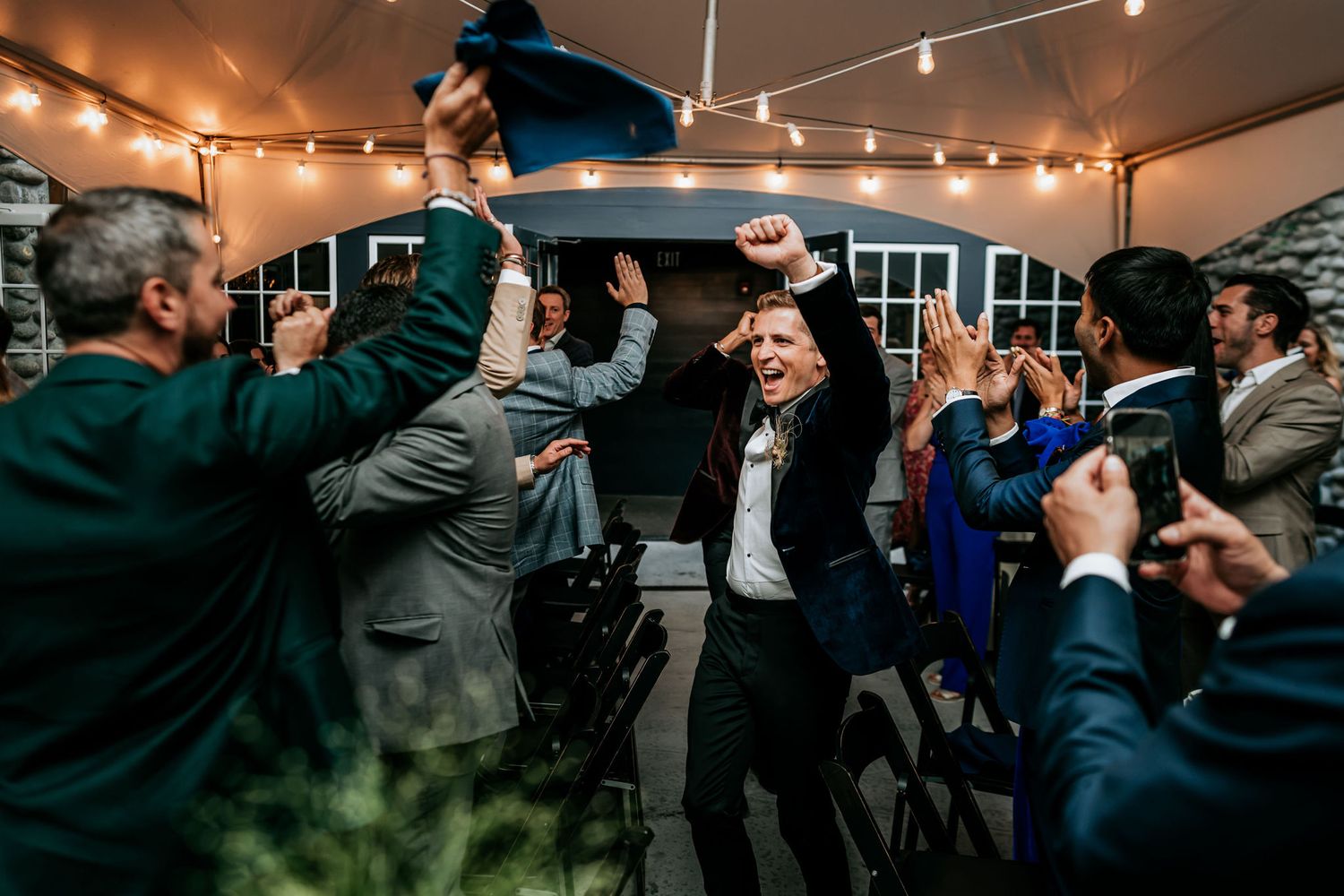 Energetic crowd celebrating at an indoor party with string lights and festive atmosphere.