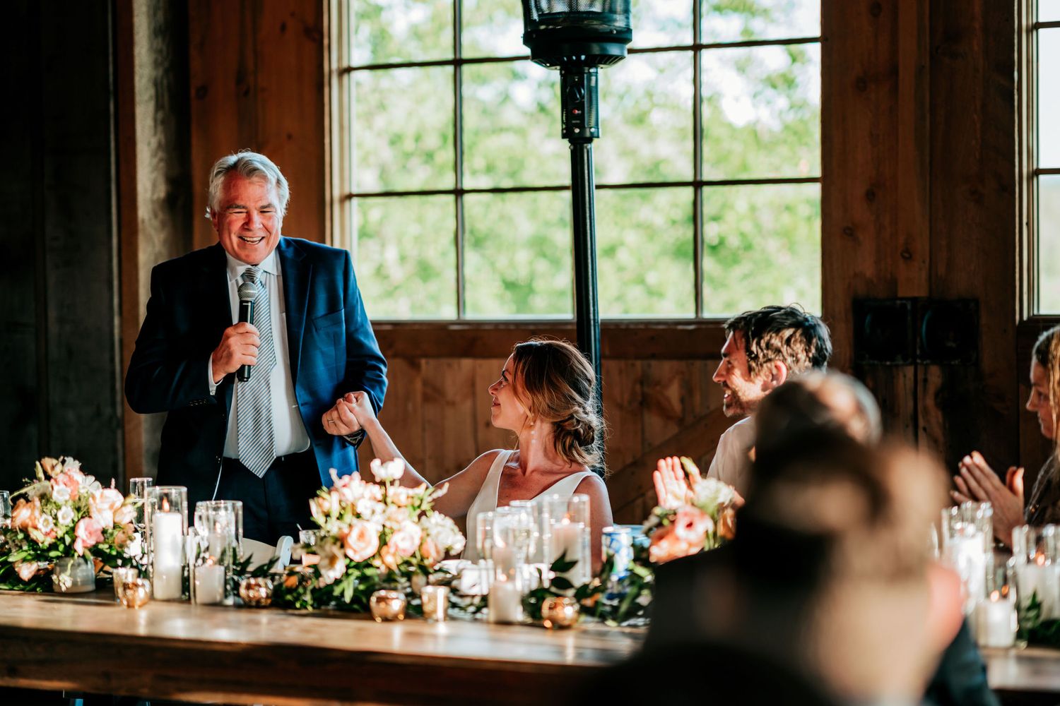 A speaker shares stories during a reception dinner in a rustic venue with natural lighting.