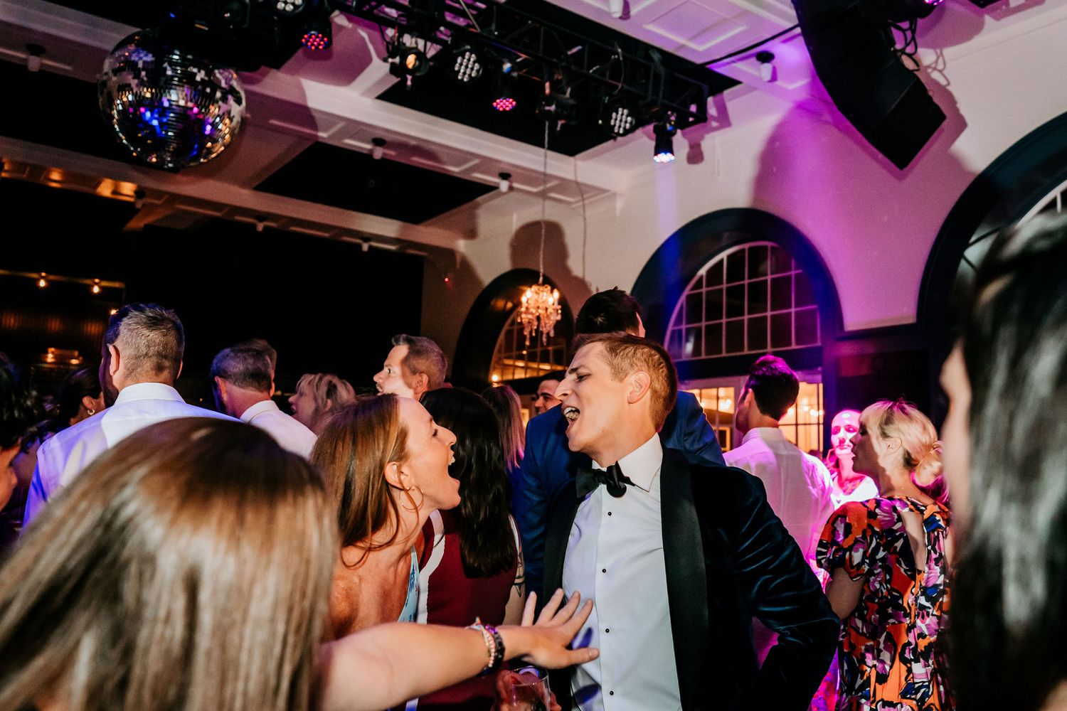 Wedding reception dance floor filled with celebrating guests under purple mood lighting.