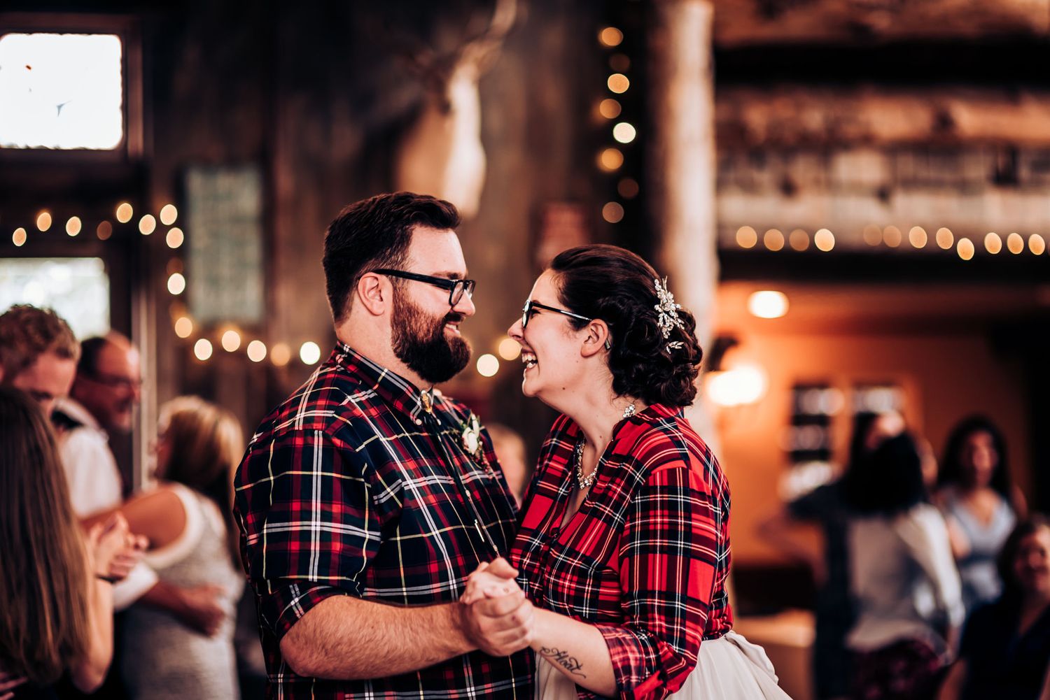 Dancing pair in matching plaid shirts sharing a romantic moment at an indoor celebration.