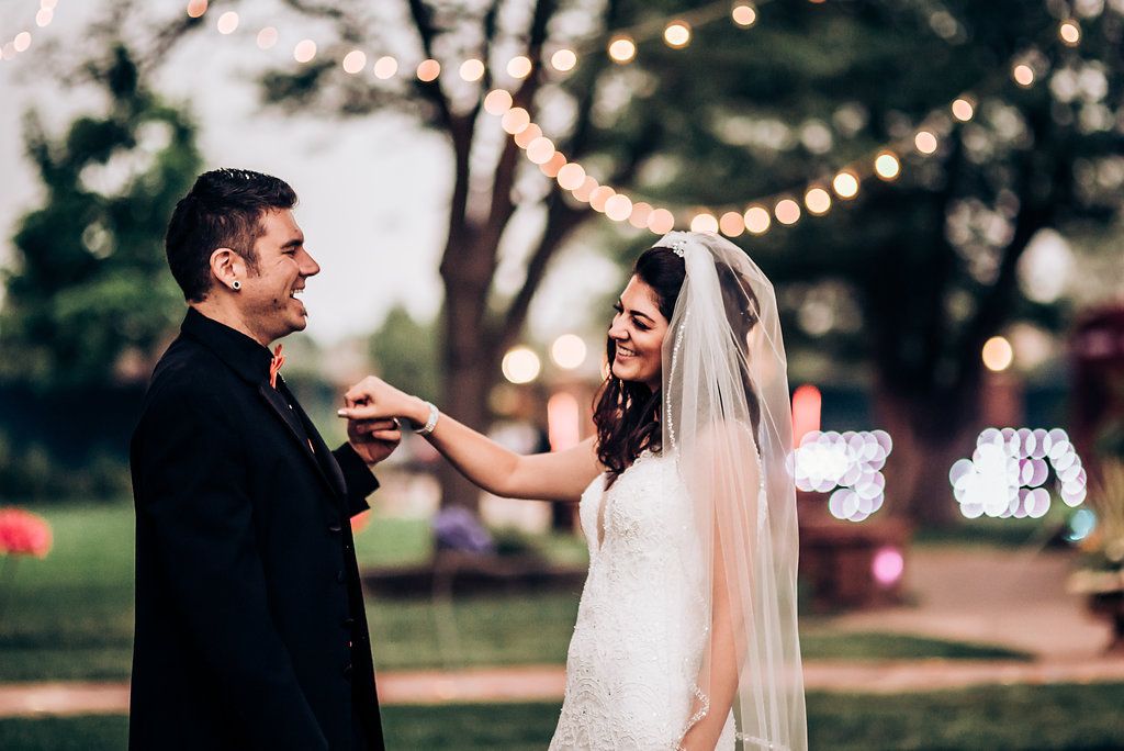 A joyful wedding moment under string lights as couple dances at dusk.