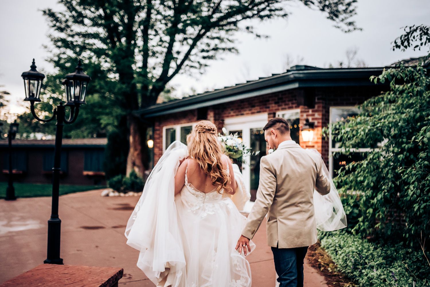 A newlywed couple walking along a charming brick path with a white bridal gown flowing behind.