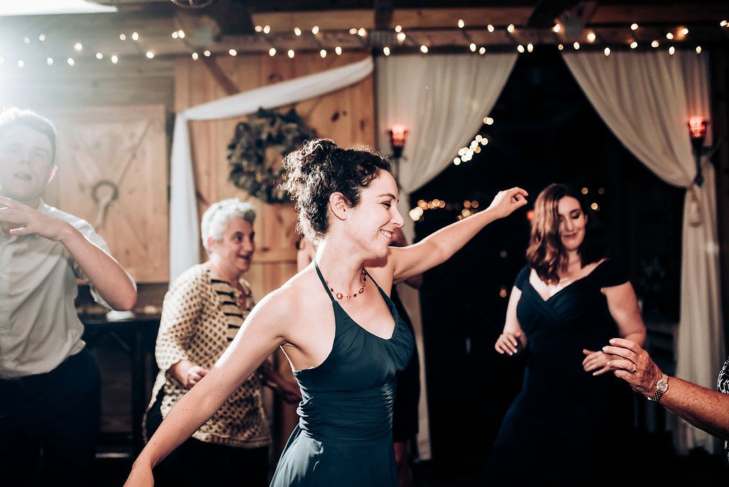 Party guests dance energetically under string lights at a wedding reception venue.