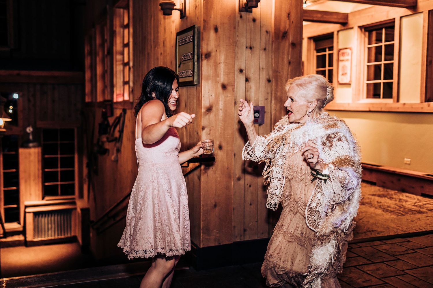 Two guests share an animated dance moment on the wooden paneled dance floor at a celebration.