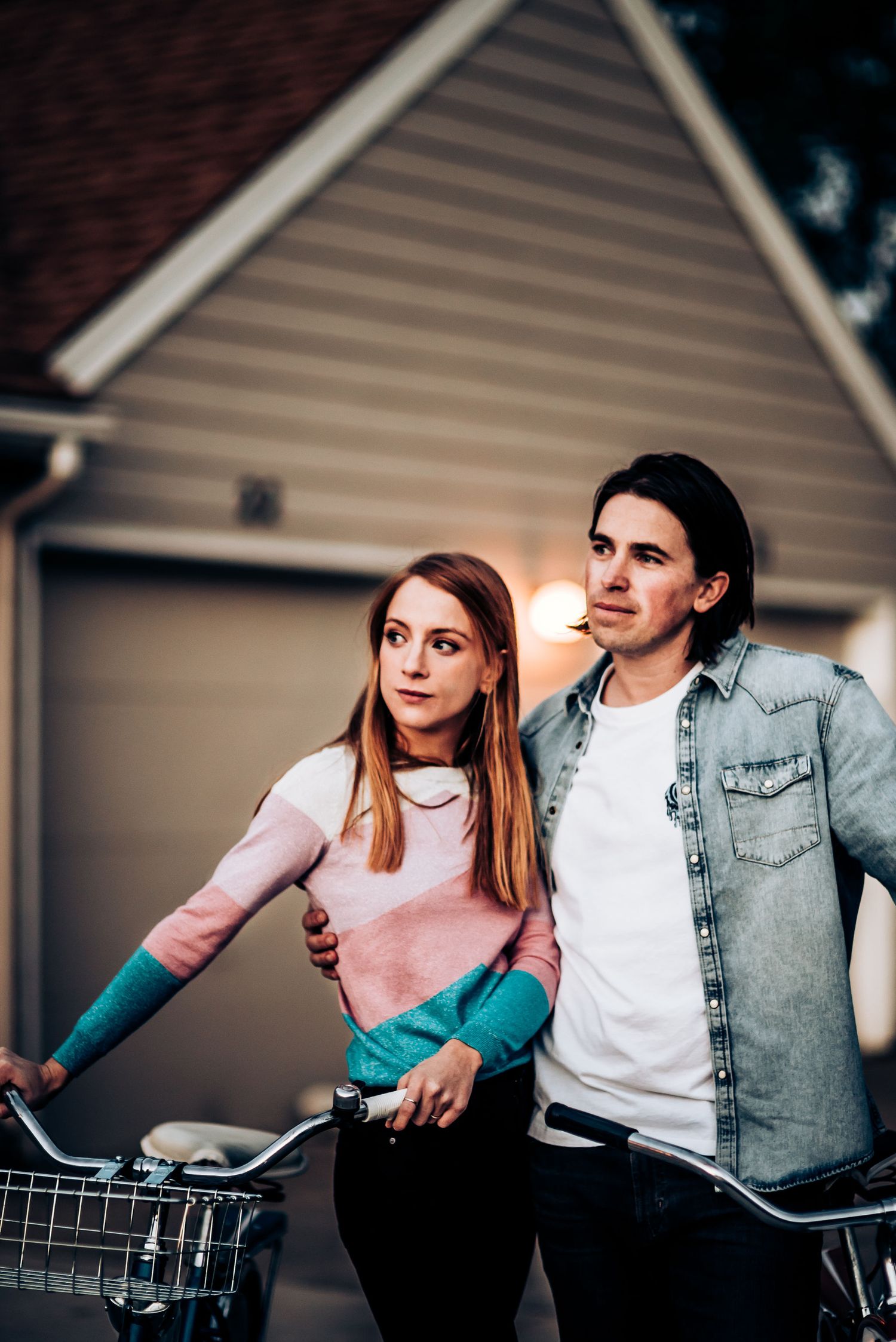 A couple poses with bicycles outside their home wearing casual attire.