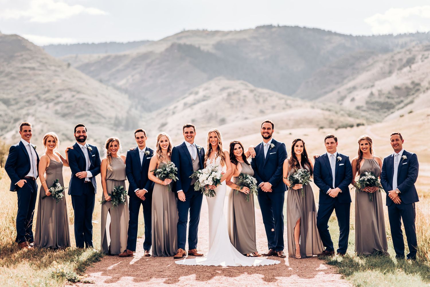 Wedding party stands together on stone path with mountain vista behind them.