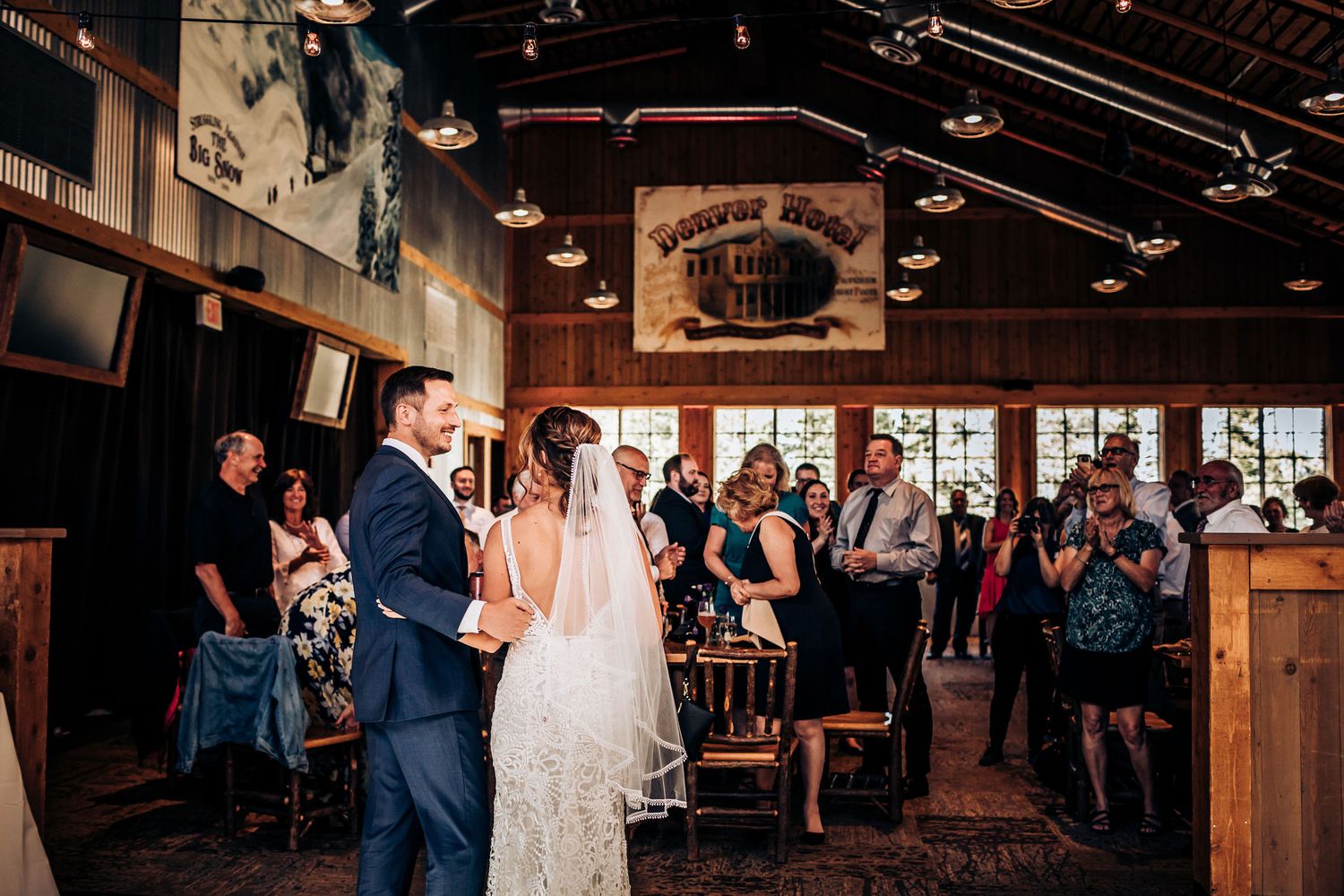 Wedding celebration in a rustic wood-paneled venue with guests standing and applauding.