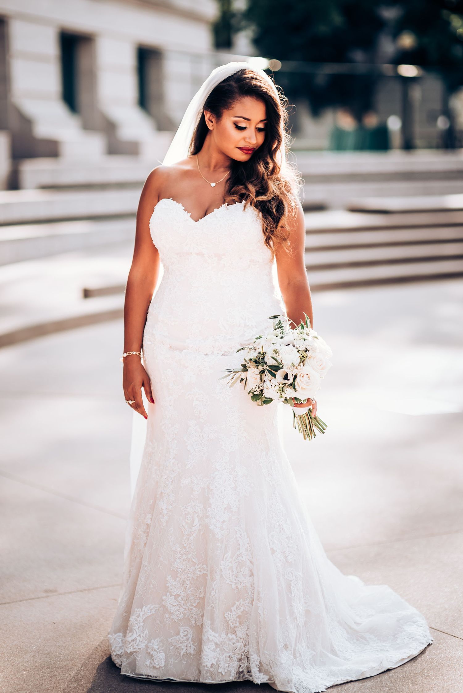 Full-length portrait of bride in fitted lace wedding dress holding white bouquet.