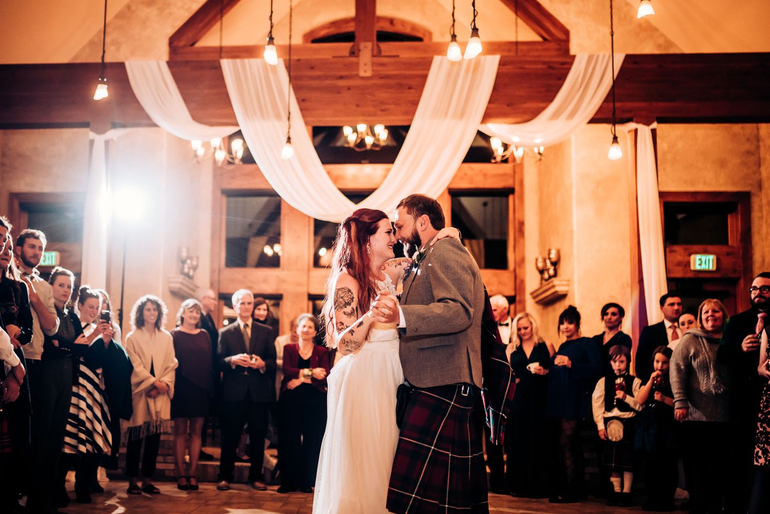 Couple shares tender moment during first dance at rustic venue with draped fabric decor.
