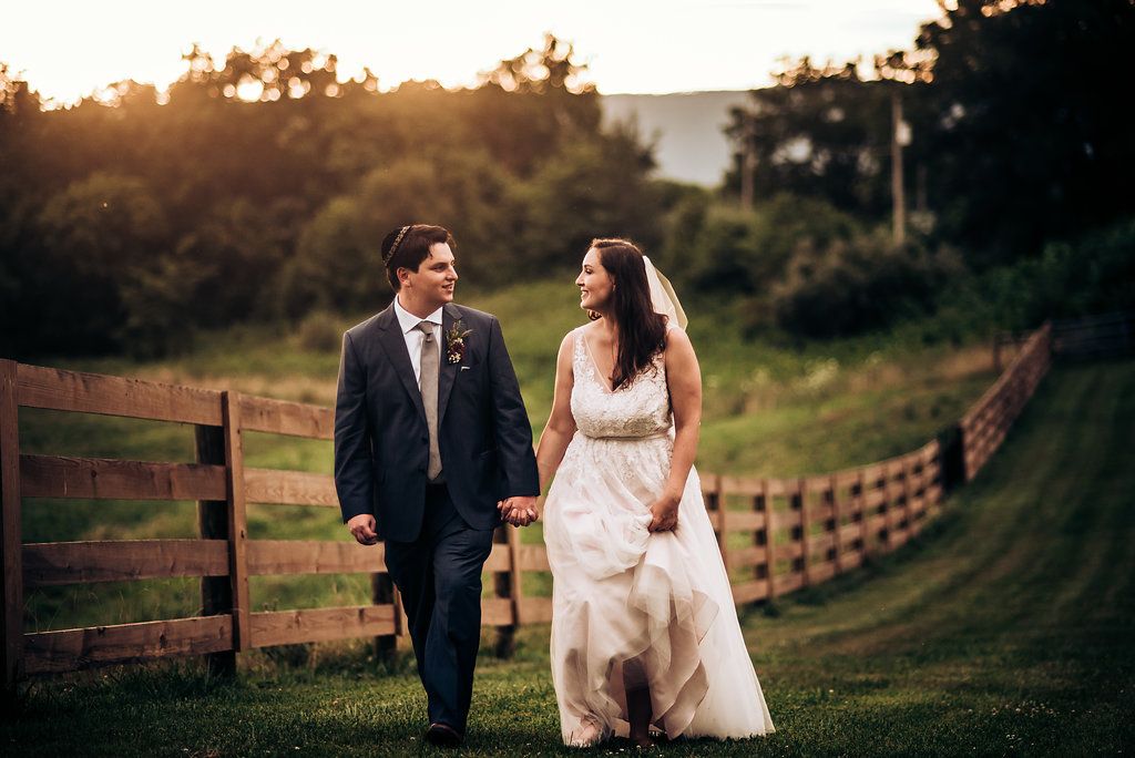 Couple walking along a rustic fence line during sunset at their wedding.