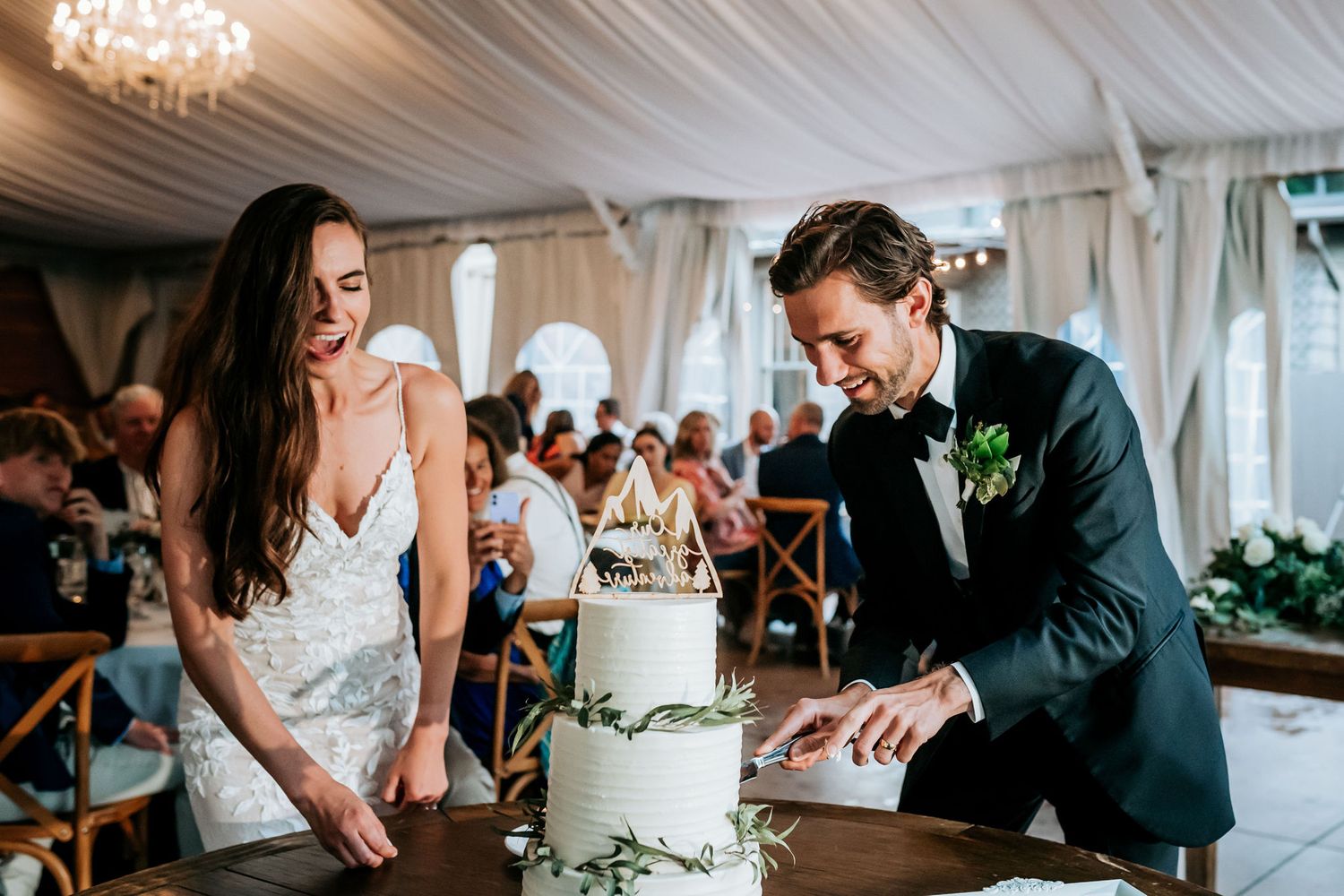 A couple cuts into their elegant white wedding cake during their reception.