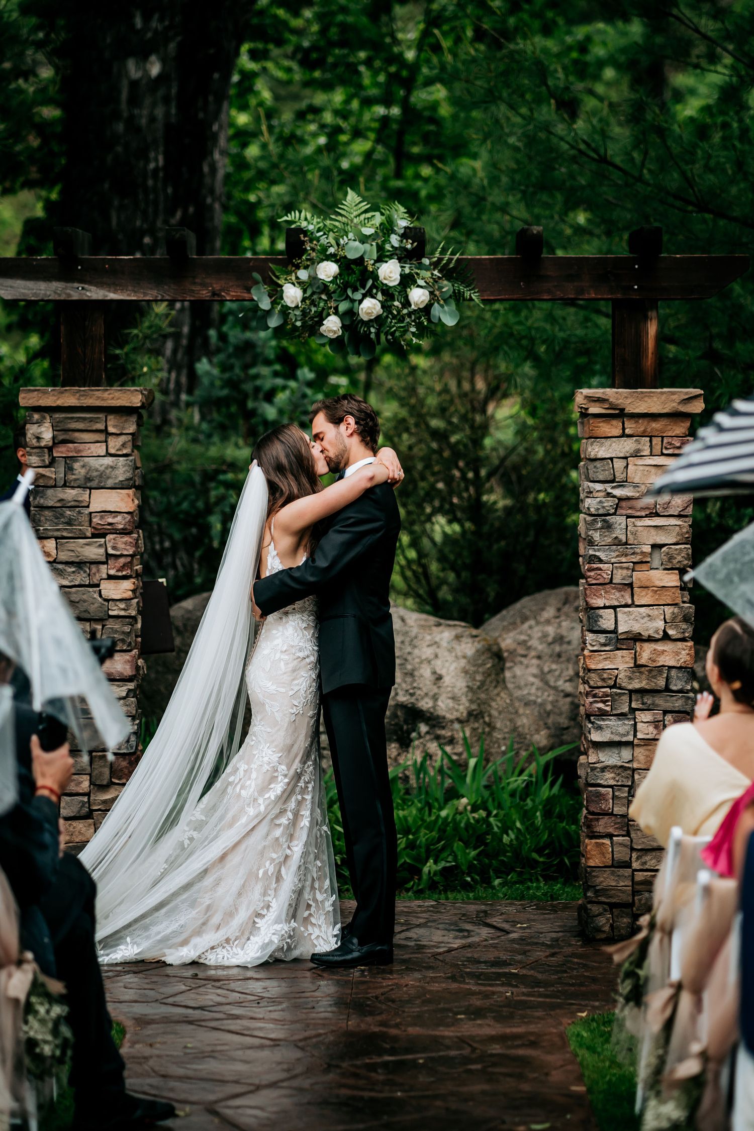 Couple shares their first kiss under a floral arch during outdoor wedding ceremony.